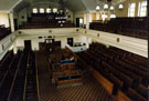 Interior of Wilson Road Synagogue showing the Reader's Desk in the centre of the hall, the mens benches and the womens gallery above and the side gallery partitioned off for women