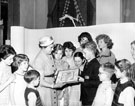 View: u02893 Mrs. Thorpe, wife of chairman of Libraries, Art Galleries and Museums Committee with John Pilley holding award for best decorated Childrens Library, Firth Park Branch Library, Christmas 1958