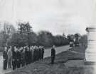 View: arc06033 First World War reunion visit (to Ypres, Belgium?) featuring group of veterans lined up along a roadside in front of a war memorial, [c. 1930s?]