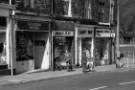 Shops on Junction Road showing (l. to r.) No. 77 Valerie Wilde, fruiterer and florist; No. 79 Hugh's News, newsagents; No. 81 Candy Bar, confectioners and No. 83 Maureen's Boutique [and Maureen Birtles Driving School] c. 1970s